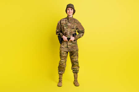 Full length portrait of charming satisfied girl standing hands hold tactical belt isolated on yellow color backgroundの写真素材