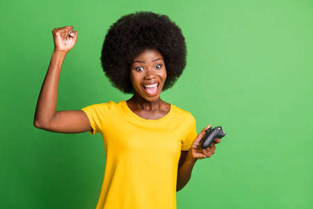 Photo of amazed victorious young afro american woman raise fist hold joystick isolated on green...