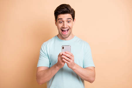 Portrait of nice cheerful focused guy blogger influenzer using device having fun isolated over beige pastel color backgroundの写真素材