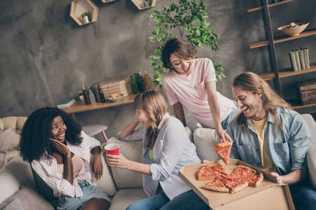 Photo portrait of friends sitting on couch eating sharing pizza talking on weekendsの写真素材