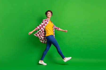 Full size profile photo of sweet funky girl walking wear jeans shirt sneakers isolated on green color backgroundの写真素材