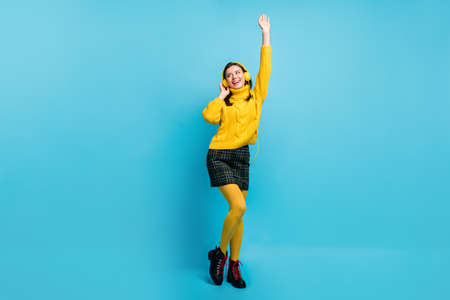 Full length photo of cute pretty young woman dressed yellow pullover earphones rising hand arm dancing isolated blue color backgroundの写真素材