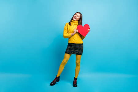 Full length photo of shiny adorable young lady wear yellow sweater holding red heart isolated blue color backgroundの写真素材