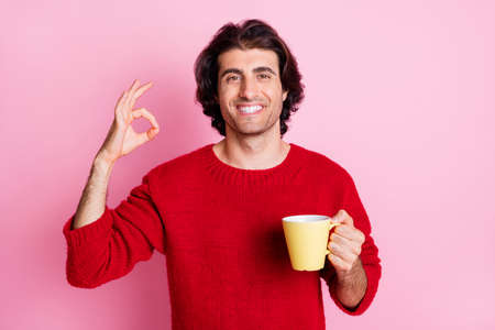 Portrait of nice content cheery guy drinking caffeine showing ok-sign ad isolated over pink pastel...