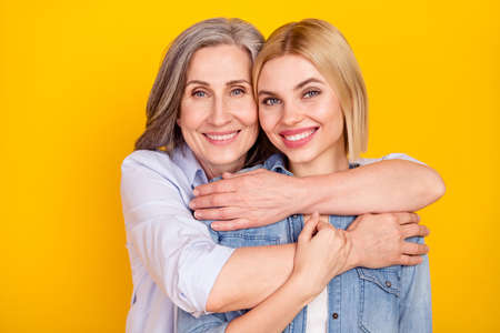Photo portrait of mother and daughter smiling hugging holding hands isolated vivid yellow color backgroundの写真素材