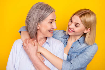 Photo portrait of mother and daughter embracing looking on each other holding hands isolated vibrant yellow color backgroundの写真素材