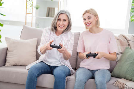 Photo of funky happy young woman and old lady sit couch play video game indoors inside house home flatの写真素材