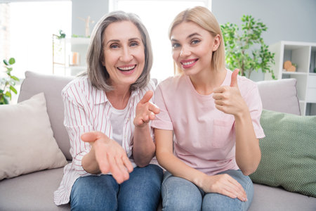 Photo of charming grey haired blonde women smile sit sofa talk make thumb-up inside home house...