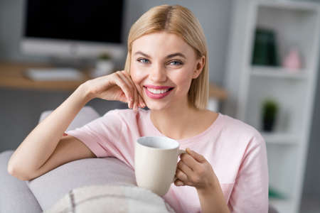 Photo of happy charming nice pretty young woman sit sofa drink coffee mug indoors inside house homeの写真素材