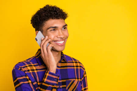 Profile portrait of cheerful dark skin guy speak phone have good mood isolated on yellow color backgroundの写真素材