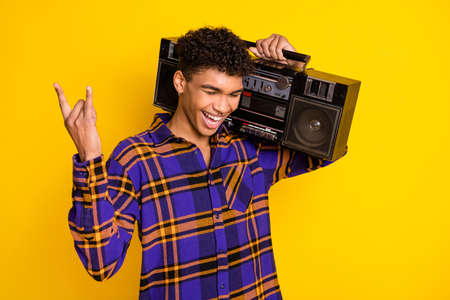 Photo portrait of handsome guy smiling keeping boom box showing heavy metal isolated on vivid yellow color backgroundの写真素材