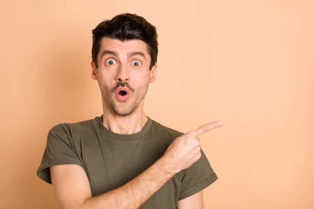 Photo of shocked guy open mouth direct finger empty space wear green t-shirt isolated beige color backgroundの写真素材