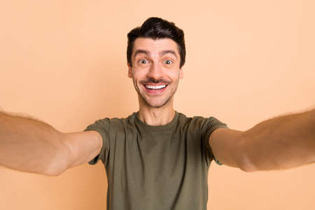 Photo portrait of guy smiling cheerful happy taking selfie keeping camera isolated on pastel beige...