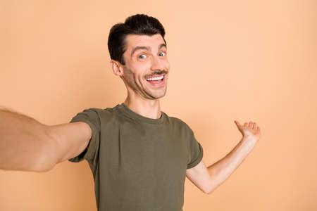 Photo of cheerful positive guy make selfie hand demonstrate empty space wear green t-shirt isolated...