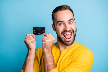 Photo of young handsome excited crazy smiling cheerful man showing credit card isolated on blue...