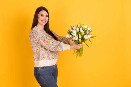 Profile side photo of attractive cheerful young lady give flowers tulips empty space isolated on yellow color backgroundの写真素材
