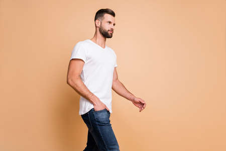 Profile side view portrait of attractive serious macho guy walking copy space isolated over beige...