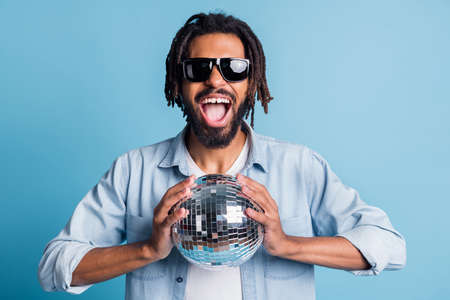 Portrait of nice cheerful cool guy holding in hands glossy disco ball having fun isolated over bright blue color backgroundの写真素材