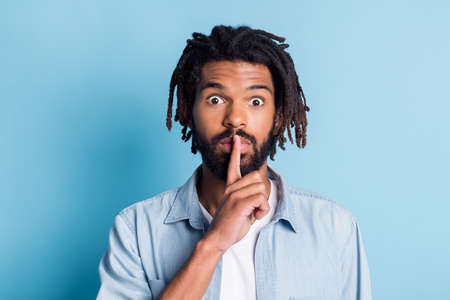 Portrait of nice suspicious guy showing shh sign dont speak isolated over vibrant blue color...