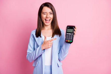 Photo of young attractive cheerful smiling positive successful female wink pointing finger terminal isolated on pink color backgroundの写真素材