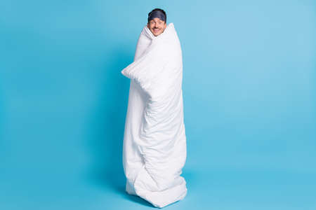 Full length photo portrait of excited smiling man wrapped in blanket isolated on vivid blue colored backgroundの写真素材