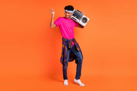 Full body photo of charming young dark skin man hold boombox wear shirt on waist isolated on orange color backgroundの写真素材