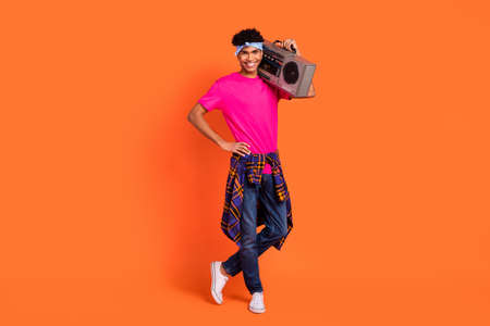 Full length body size photo of confident guy smiling keeping retro boom box isolated on bright orange color backgroundの写真素材