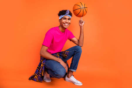 Full length body size photo guy sitting smiling spinning ball on finger isolated bright orange color backgroundの写真素材