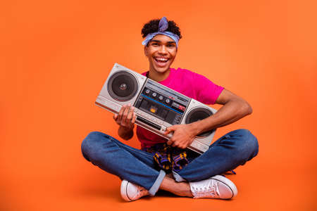 Full length body size photo of happy hipster laughing holding retro boom box isolated bright orange color backgroundの写真素材