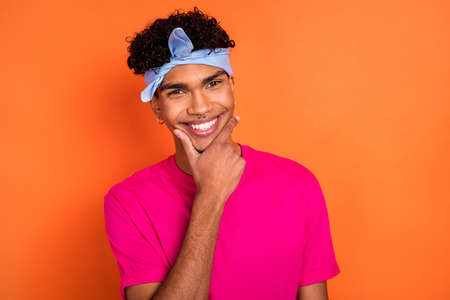 Photo portrait of smiling young guy wearing headband piercing touching chin thoughtful isolated on vivid orange color backgroundの写真素材