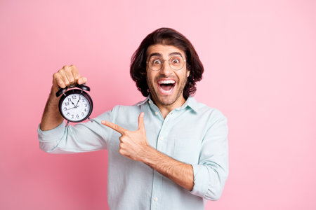 Photo of cheerful funny guy pointing clock wear spectacles blue shirt isolated on pastel pink color backgroundの写真素材