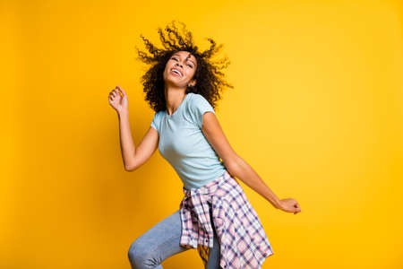 Photo of shiny sweet charming dark skin curly woman dressed blue t-shirt dancing isolated yellow color backgroundの写真素材