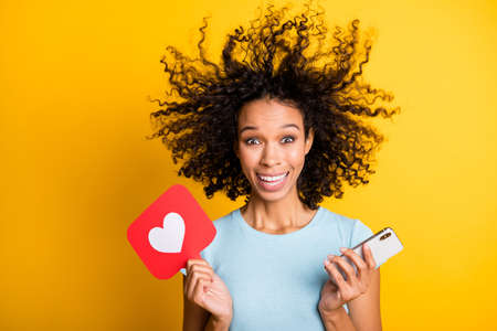 Photo of impressed dark skin curly woman dressed t-shirt holding like icon device wind blow isolated...