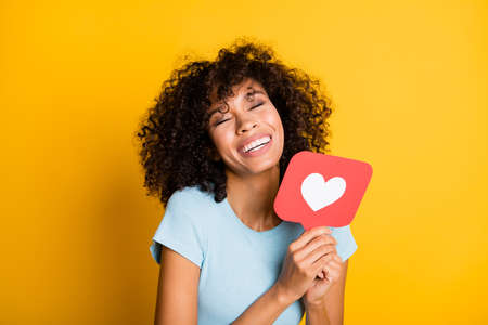 Photo of adorable cheerful dark skin curly woman dressed blue t-shirt holding like icon closed eyes...