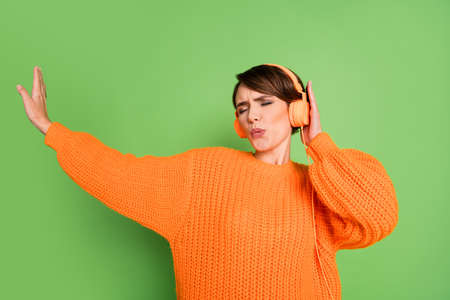 Photo of happy cute funky woman sing listen music headphones raise hand isolated on green color backgroundの写真素材