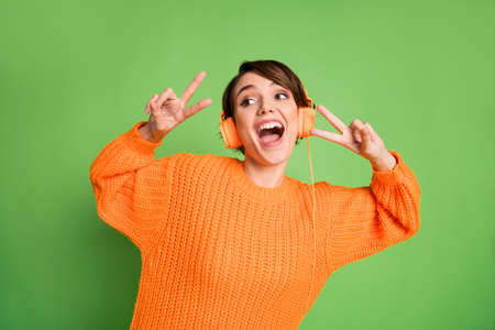 Photo of excited happy young woman wear headset show two v-signs look empty space isolated on green color backgroundの写真素材