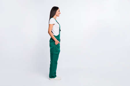 Profile photo of charming cheerful lady look empty space hand pocket wear green overall isolated white color backgroundの写真素材