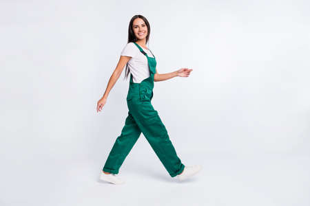 Photo of positive cheerful lady walk go beaming smile wear green overall shoes isolated white color backgroundの写真素材