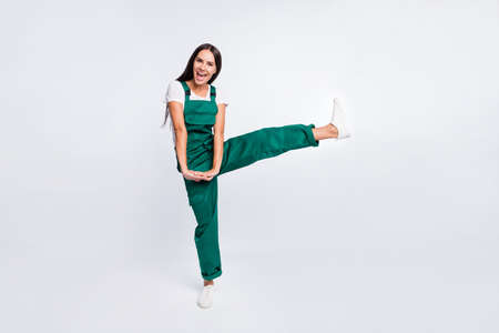 Photo of crazy party lady hold hands open mouth raise leg wear green overall sneakers isolated white color backgroundの写真素材