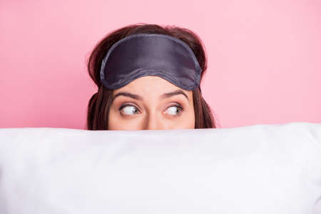 Photo portrait of woman hiding behind pillow looking to side isolated on pastel pink colored backgroundの写真素材