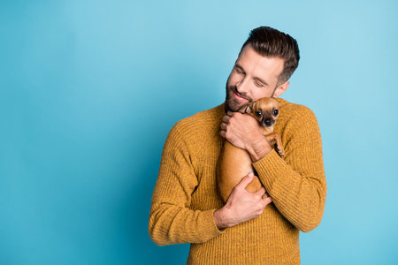 Photo of young happy dreamy positive good mood handsome man embrace chiahuahua isolated on blue color backgroundの写真素材