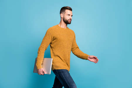 Portrait of attractive skilled guy carrying laptop walking meeting office isolated over bright blue color backgroundの写真素材