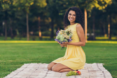 Portrait of attractive elegant cheerful girl sitting on duvet holding bouquet spending free time on fresh air outdoorの写真素材