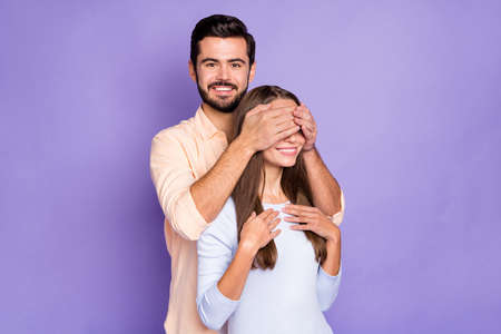 Photo of funny cheerful young spouses man cover woman eyes play game isolated on purple color backgroundの写真素材