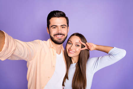 Photo of cheerful brunette man and woman make v-sign take selfie lovers isolated on violet color...