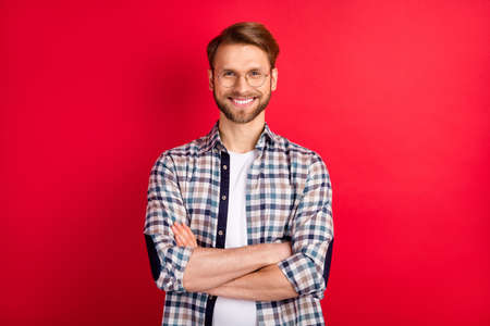 Photo of pretty confident young gentleman dressed plaid shirt spectacles hands folded smiling isolated red color backgroundの写真素材