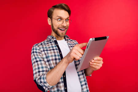 Photo of excited funny young guy wear checkered shirt glasses typing modern device big eyes isolated...