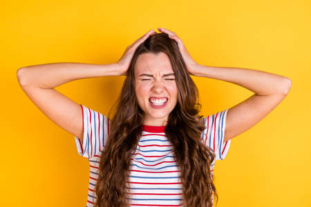 Photo of tired upset young lady dressed striped t-shirt headache arms head isolated yellow color backgroundの写真素材