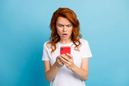 Photo portrait of offended girl holding phone in two hands isolated on pastel blue colored...