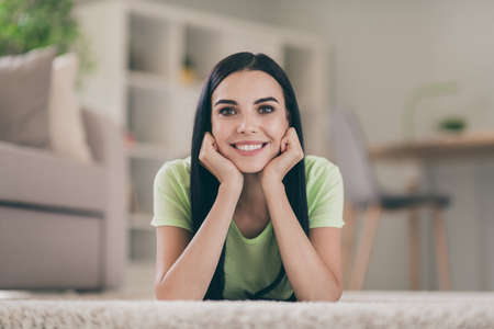 Close-up portrait of lovely cheerful long-haired brunet girl lying on carpet spending time pastime at light interior roomの写真素材